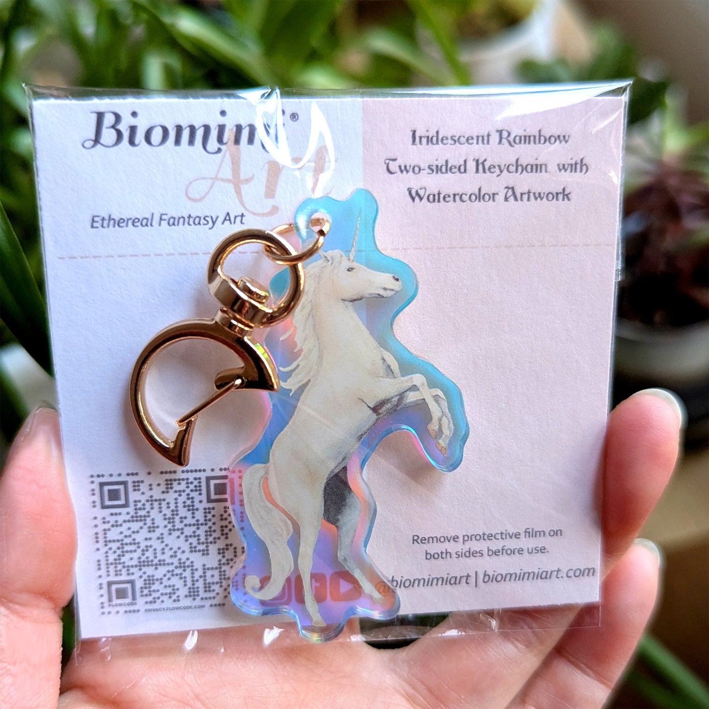 Iridescent rainbow keychain with unicorn design held in front of its packaging.